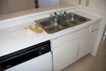 Before image of warn countertop with sink and deteriorated cabinetry.